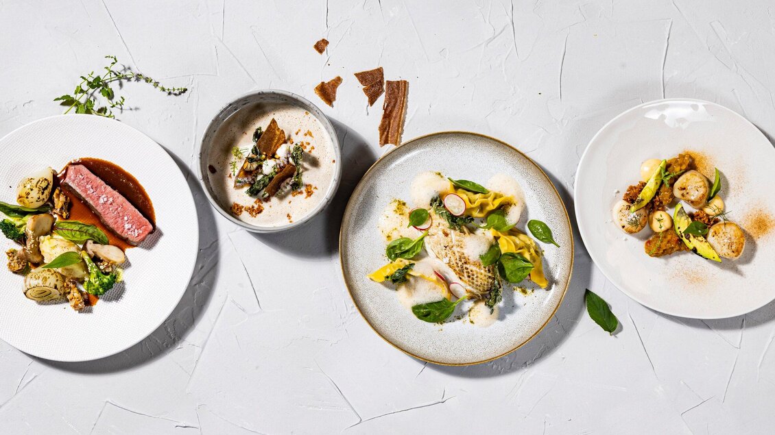 Ein ansprechend angerichtetes Menü mit vier verschiedenen Gerichten. Die Teller zeigen eine Vielfalt an Zutaten und Farben, die zum Essen einladen. | © Restaurant Schlossberg - Werner Krug