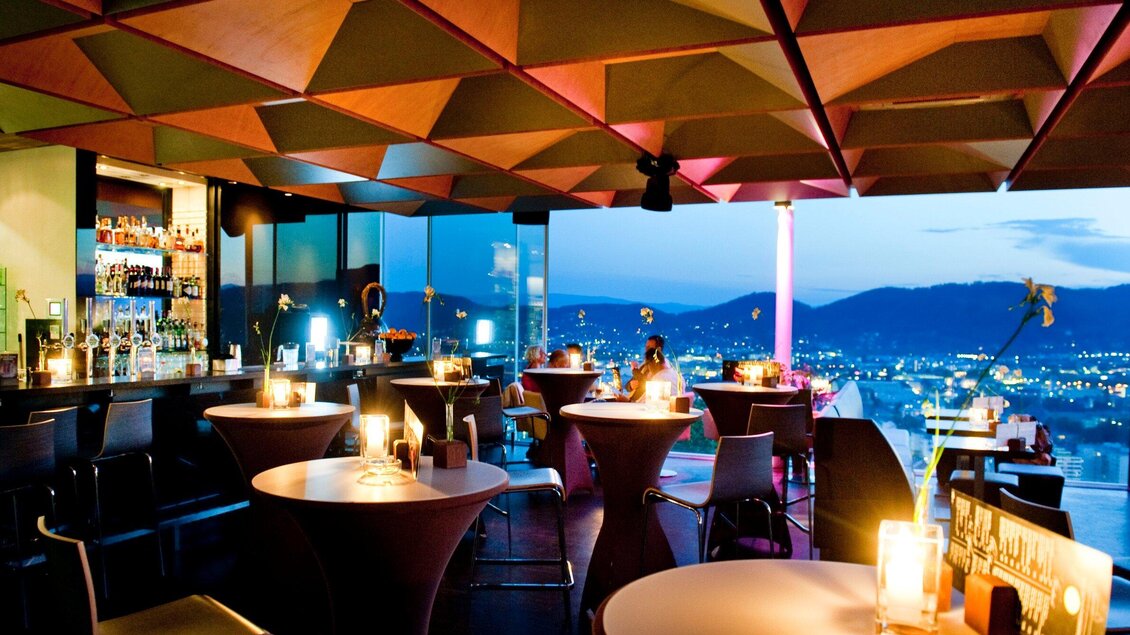 Ein modernes Restaurant mit stilvollem Design und Blick auf die Stadt. Sanftes Licht und elegante Möbel schaffen eine einladende Atmosphäre. | © Schlossberg - Werner Krug