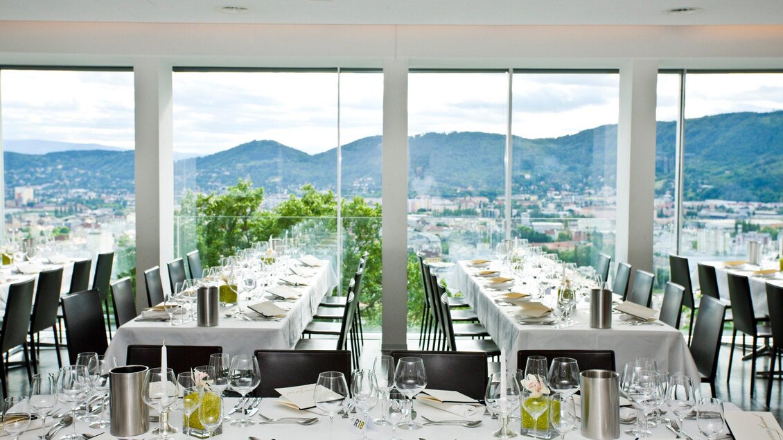 Ein elegantes Restaurant mit großen Fenstern und einem Blick auf die Berge. Die Tische sind schön eingedeckt und bereit für Gäste. | © Restaurant Schlossberg