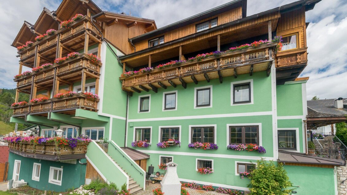 Ein farbenfrohes Gebäude im Landhausstil mit Balkonen und blühenden Pflanzen. Die Fassade ist grün, umgeben von einer gepflegten Gartenanlage. | © Restaurant Schwaiger