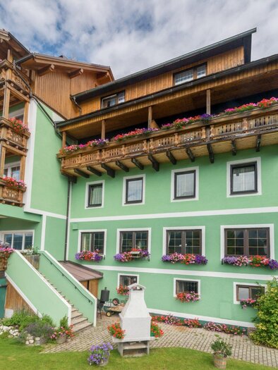 A colorful country-style building with balconies and blooming plants. The facade is green, surrounded by a well-maintained garden. | © Restaurant Schwaiger
