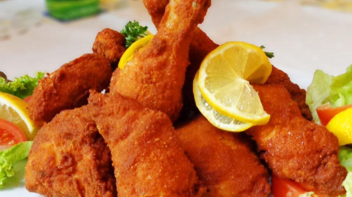 Ein Teller mit knusprigen, frittierten Hähnchenteilen, garniert mit frischem Salat und Zitronenscheiben. Das Gericht sieht appetitlich und einladend aus. | © Restaurant Schwaiger