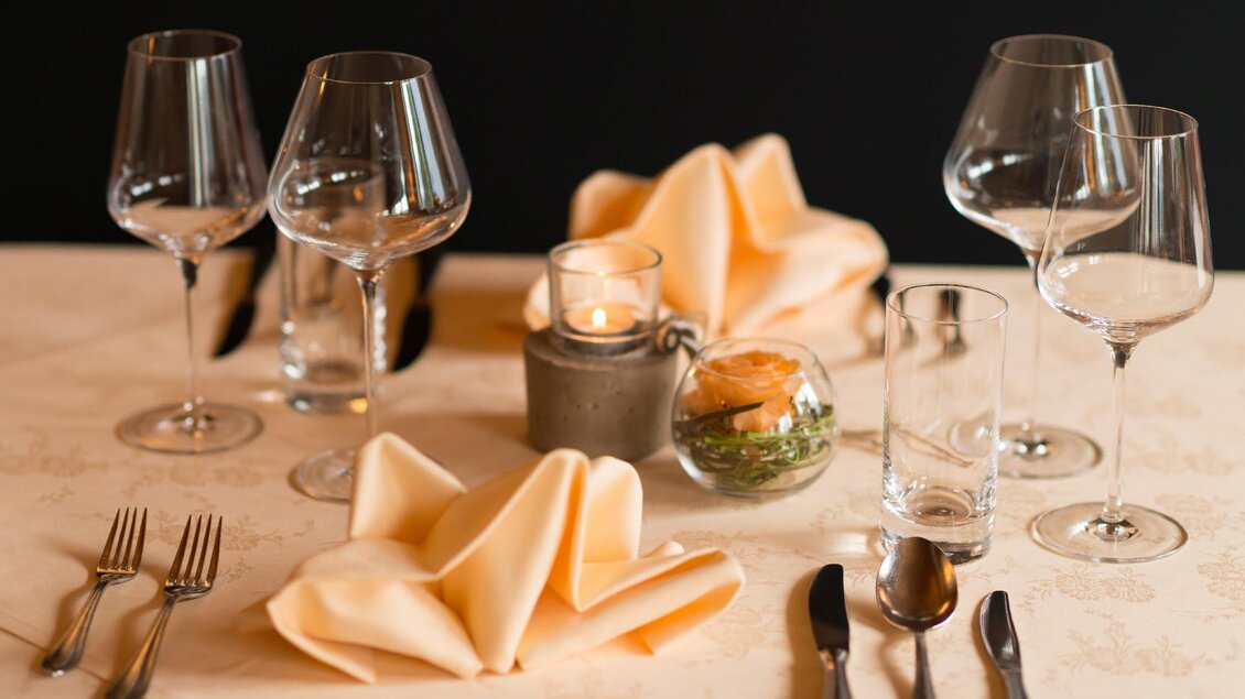 Ein eleganter Tisch gedeckt mit Weingläsern und Besteck. Auf dem Tisch befindet sich eine Kerze und eine kleine Blumendekoration. | © Restaurant Schwaiger