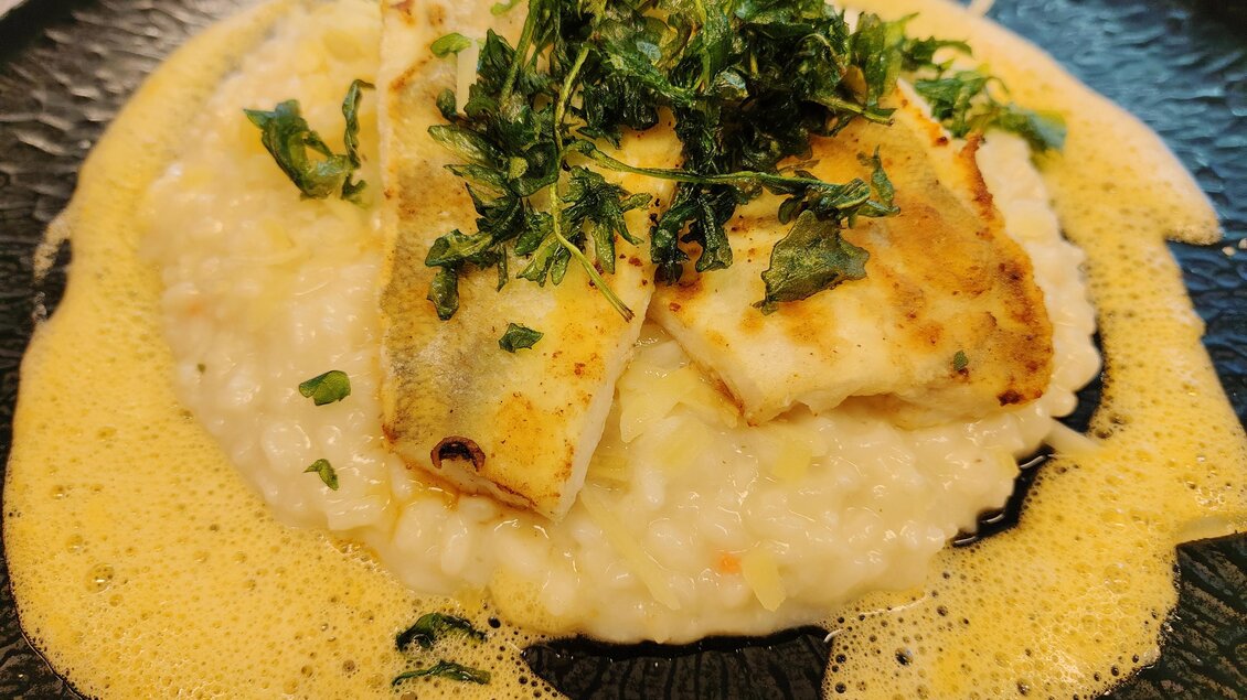 Fischfilet auf cremigem Risotto, umgeben von Schaum und garniert mit frittierten Kräutern im Restaurant Steiramichl in den Stadtsälen Voitsberg.  | © © Steiramichl