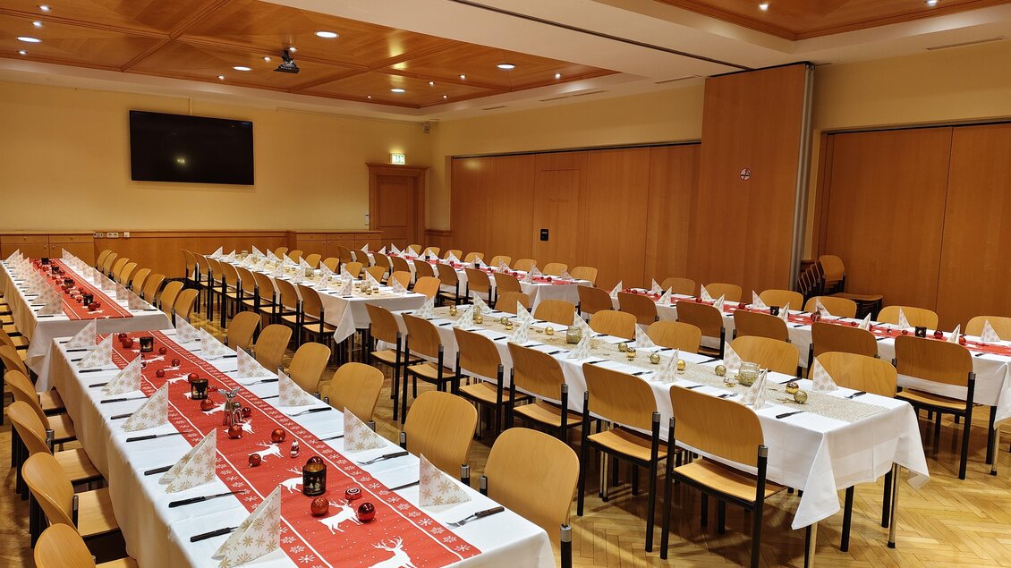 Großer Veranstaltungssaal mit weihnachtlich gedeckten Tischen und rotem Tischläufer in den Stadtsälen Voitsberg.  | © © Steiramichl