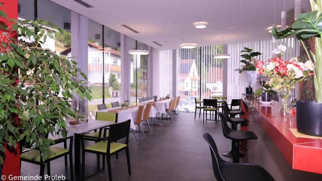 Ein modernes Café mit großen Fenstern und Blick ins Grüne. Die Einrichtung ist hell und freundlich mit Pflanzen und Farbdetails. | © Gemeinde Proleb