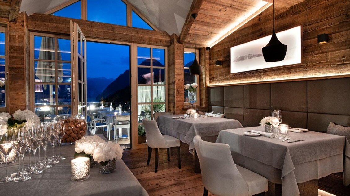 Ein elegantes Restaurant mit Holzwänden und gedämpftem Licht. Die Tische sind stilvoll gedeckt und bieten einen Blick auf die Abendlandschaft. | © Mondi Resort