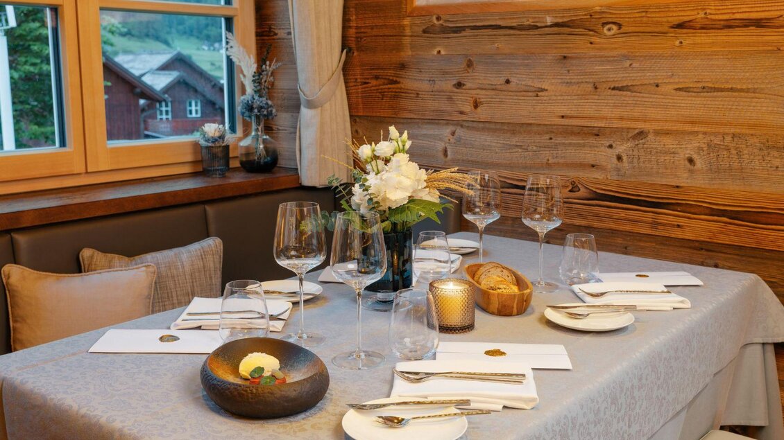 Ein elegant gedeckter Tisch in einem gemütlichen Raum mit Holzverkleidung. Frische Blumen und Kerzen sorgen für eine einladende Atmosphäre. | © Mondi Resort