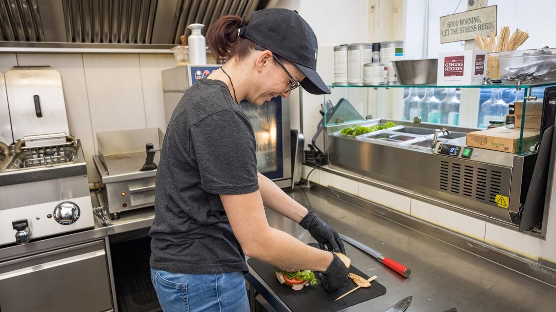 Eine Köchin bereitet Sandwiches in einer modernen Küche vor. Sie trägt Handschuhe und konzentriert sich auf ihre Arbeit. | © Netzwerk Kulinarik wildbild