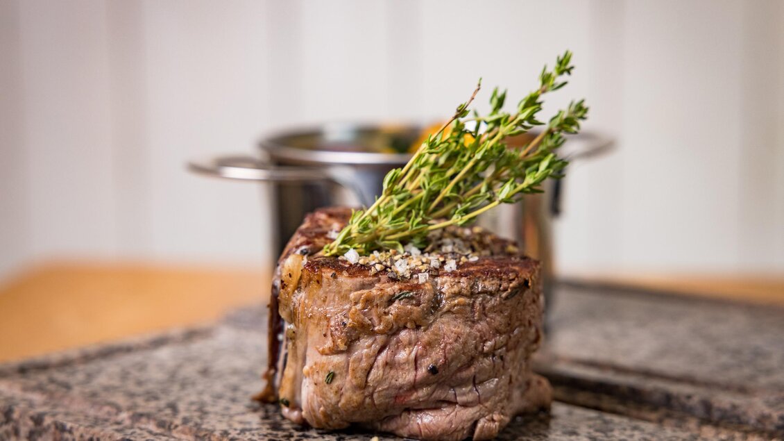 Ein saftiges Stück Fleisch mit frischen Kräutern auf einem Granitblock. Im Hintergrund steht ein Topf, bereit zum Kochen. | © Netzwerk Kulinarik wildbild