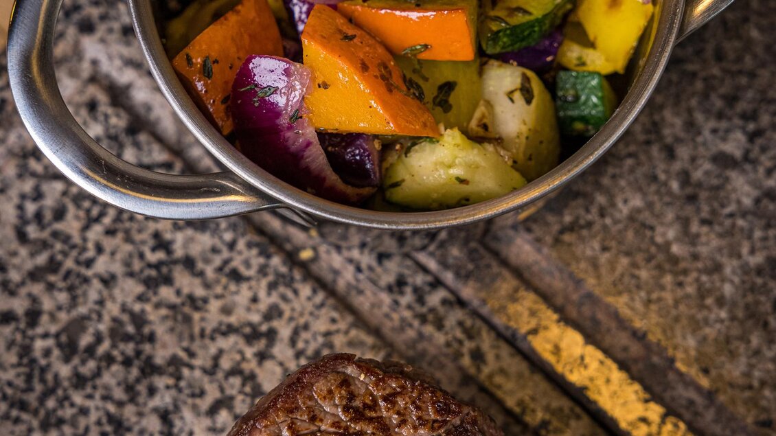 Ein schmackhaftes Gericht mit einem Stück Fleisch und buntem Gemüse in einer kleinen Metallschüssel. Das Gemüse ist frisch und aromatisch zubereitet. | © Netzwerk Kulinarik wildbild