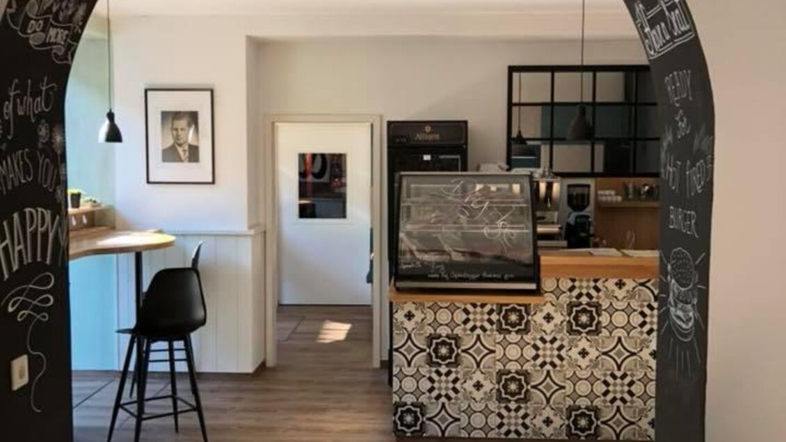 Ein moderner Raum mit einem eleganten Thekenbereich und einem Holzfußboden. Die Wände sind kreativ bemalt und es gibt einen offenen Durchgang. | © Walter.Grill.Burger