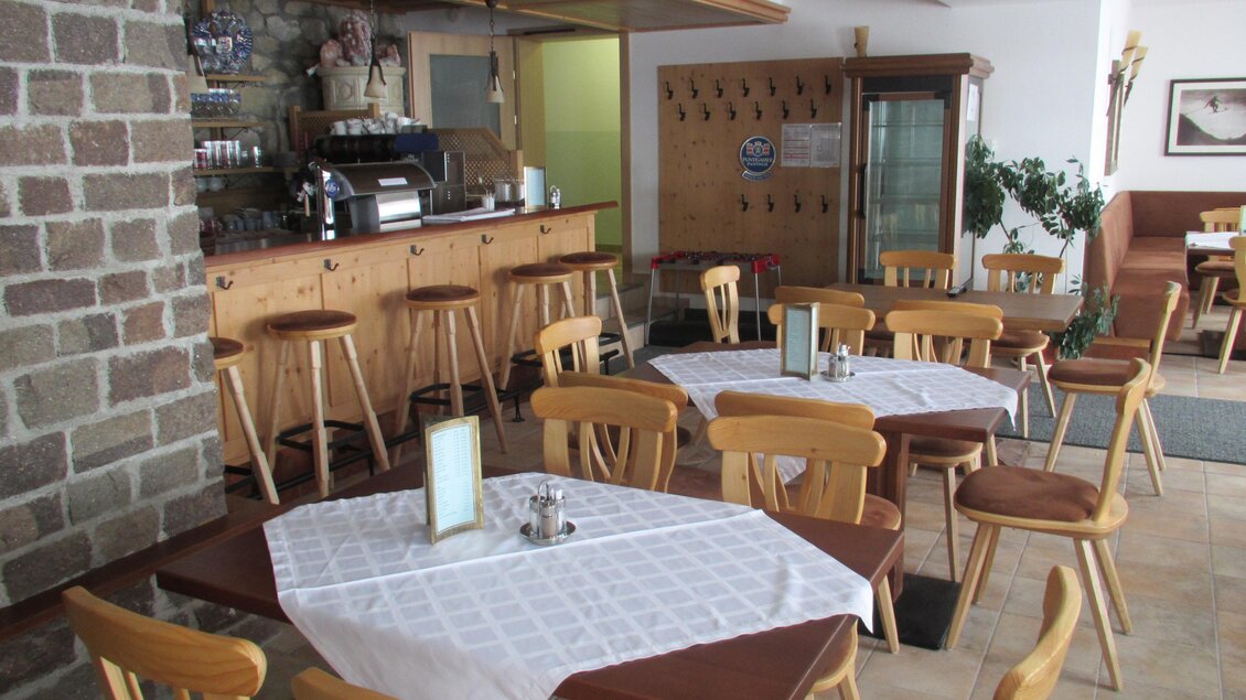 Ein gemütliches Café mit Holzstühlen und Tischen. Im Hintergrund befindet sich eine Theke mit Kaffeezubereitung. | © Hotel Alpen Arnika