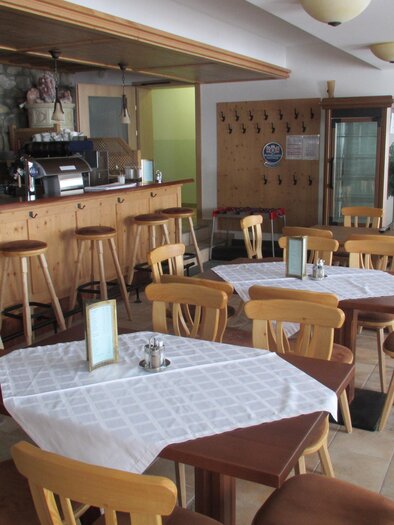 Ein gemütliches Café mit Holzstühlen und Tischen. Im Hintergrund befindet sich eine Theke mit Kaffeezubereitung. | © Hotel Alpen Arnika