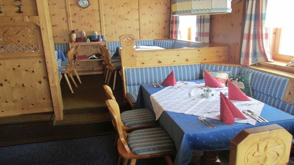 Ein gemütliches Restaurant mit Holzvertäfelung und blauen Tischdecken. Der Tisch ist gedeckt mit roten Servietten und Besteck. | © Hotel Alpen Arnika