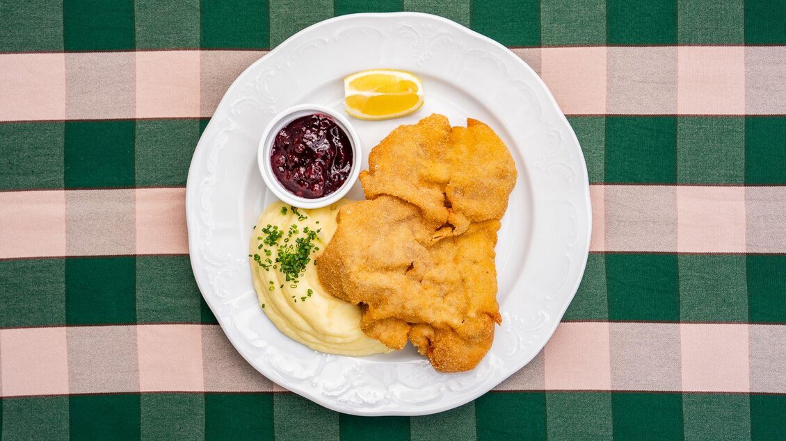 Ein Teller mit knusprigem Fisch, serviert mit püriertem Kartoffeln und Preiselbeermarmelade. Dazu gibt es zwei Zitronenscheiben. | © Hotel Alpen Arnika