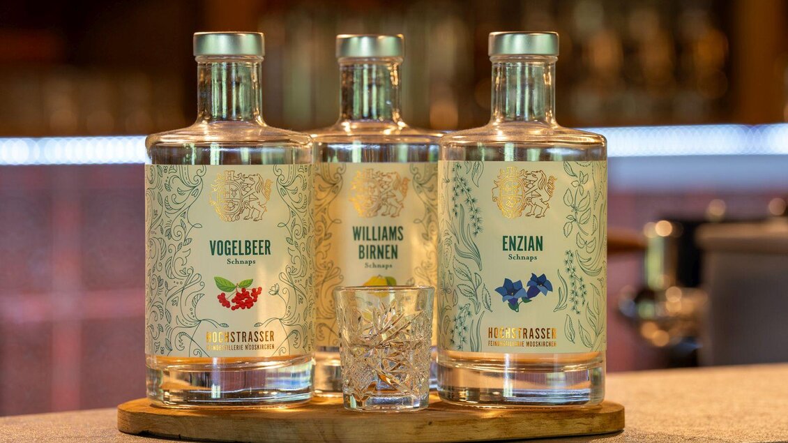 Drei Flaschen mit Schnaps stehen auf einem Holztablett. Die Etiketten zeigen die Sorten Vogelbeer, Williams Birnen und Enzian. | © Hotel Alpen Arnika