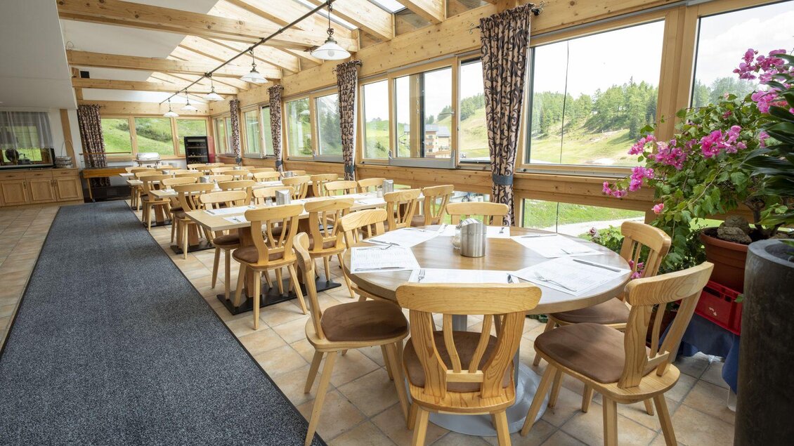 Ein einladendes Restaurant mit Holzstühlen und großen Fenstern. Der Raum ist hell und freundlich, umgeben von Pflanzen und einer schönen Aussicht. | © Hotel Alpen Arnika