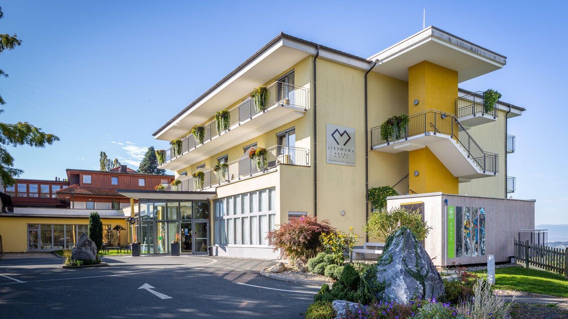 Ein modernes Hotelgebäude mit hellgelber Fassade und mehreren Etagen. Es liegt in einer grünen Umgebung und hat große Fenster sowie einen einladenden Eingangsbereich. | © Werbelechner