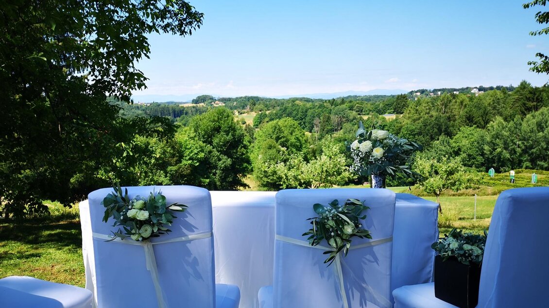 Ein schöner Blick auf eine grüne Landschaft mit Bäumen und Hügeln. Im Vordergrund sind weiße Stühle mit blumigen Dekorationen. | © Hotel Liebmann