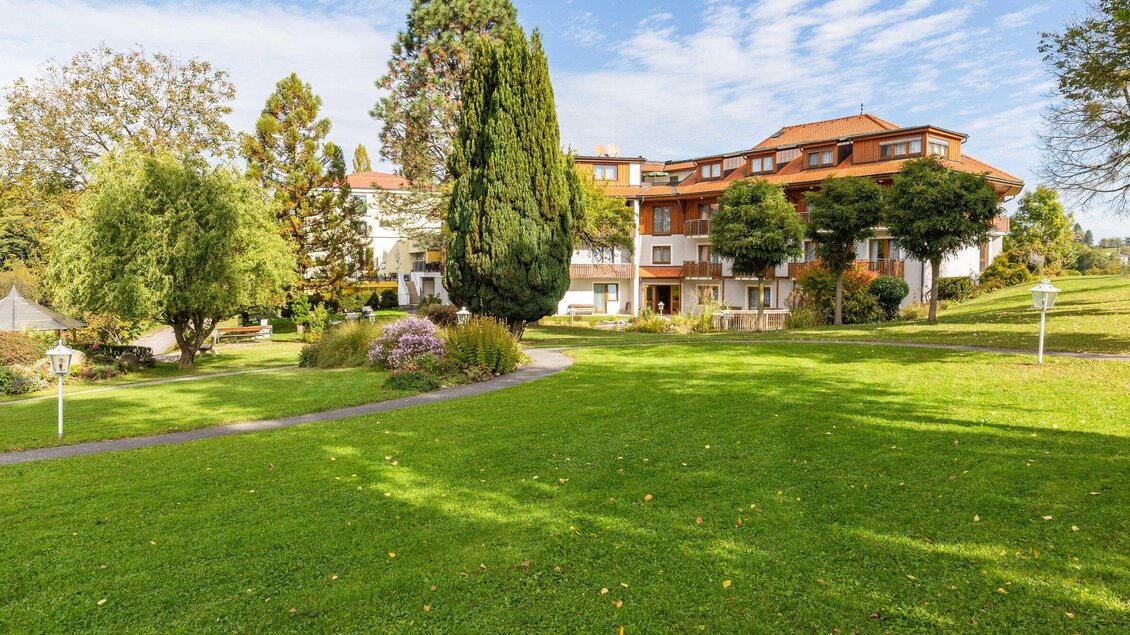 Eine großzügige Grünfläche mit einem gepflegten Garten und verschiedenen Bäumen. Im Hintergrund ist ein mehrstöckiges Gebäude zu sehen, umgeben von schöner Natur. | © Werbelechner