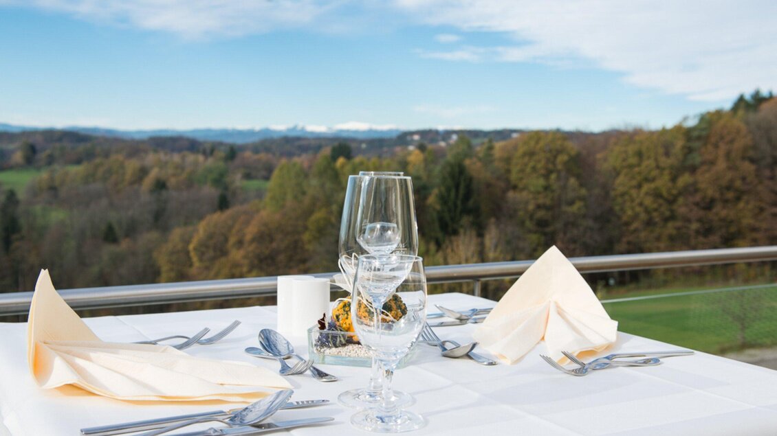 Ein elegant gedeckter Tisch mit Glas und Besteck, der eine schöne Aussicht auf eine grüne Landschaft bietet. Die Tischdecke ist weiß mit dekorativen Servietten und einem kleinen Arrangement. | © Ulf Thausing