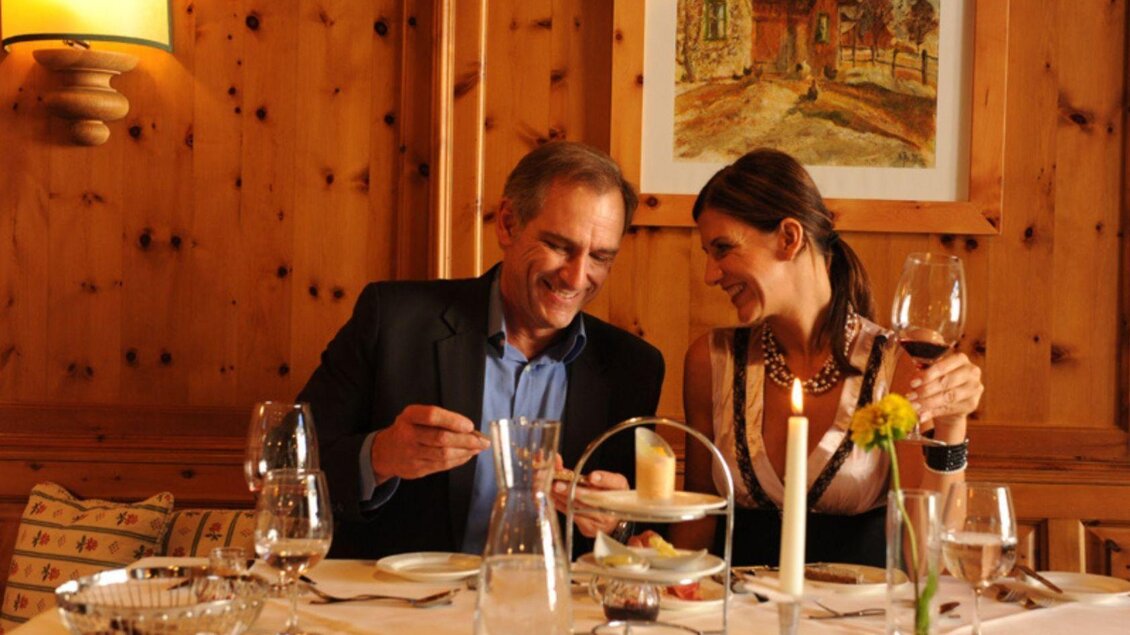 Ein romantisches Dinner in einem gemütlichen Restaurant. Ein Paar genießt Essen und Trinken in einer warmen, holzverkleideten Umgebung. | © SPA Hotel Erzherzog Johann, Bad Aussee, Restaurant (c) Ralf Tornow
