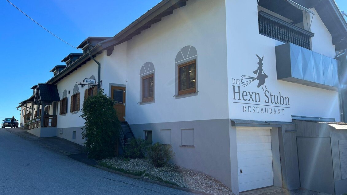 Ein rustikales Restaurantgebäude namens "Hexn Stubn" am Hang. Es hat eine helle Fassade und viele Fenster, umgeben von einer ruhigen Umgebung. | © Familie Wachmann