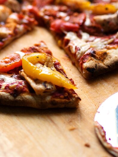 A delicious pizza with spicy pepper pieces on a wooden board. Some pieces are already cut out, and a pizza cutter lies beside it. | © Brett Jordan