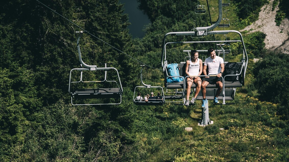 Eine Seilbahn fährt über eine grüne Landschaft. Zwei Personen sitzen entspannt in der Gondel. | © Armin Walcher