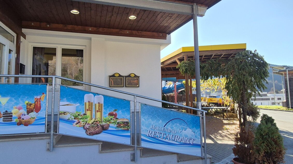 Ein einladendes Restaurant mit einer Terrasse. Die Fassade zeigt ein attraktives Werbebanner mit leckeren Gerichten und Getränken. | © Tourismusverband Murau