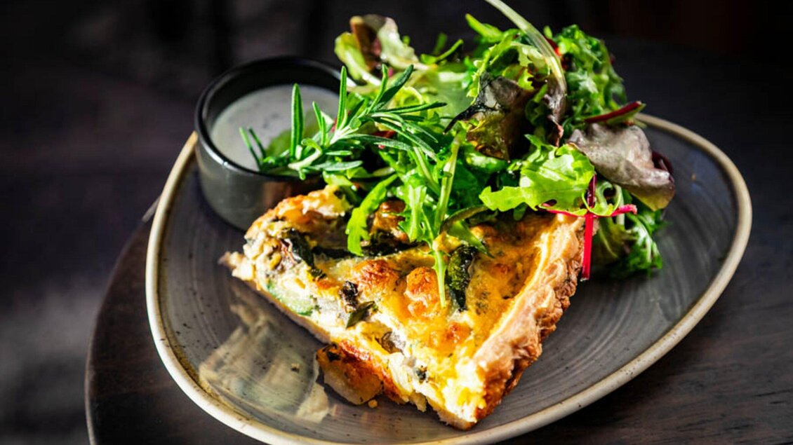 Ein Stück Quiche mit frischem Gemüse und einer Beilage aus knackigem Salat. Dazu serviert wird ein kleines Schälchen mit Dressing. | © Ristorante Trenta