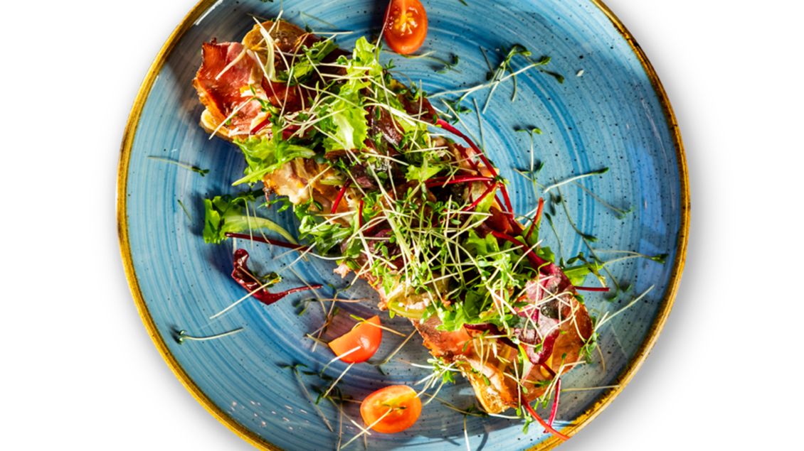 Ein kunstvoll angerichtetes Gericht auf einem blauen Teller. Es enthält Fisch, frisches Gemüse und einige Cocktailtomaten. | © Ristorante Trenta