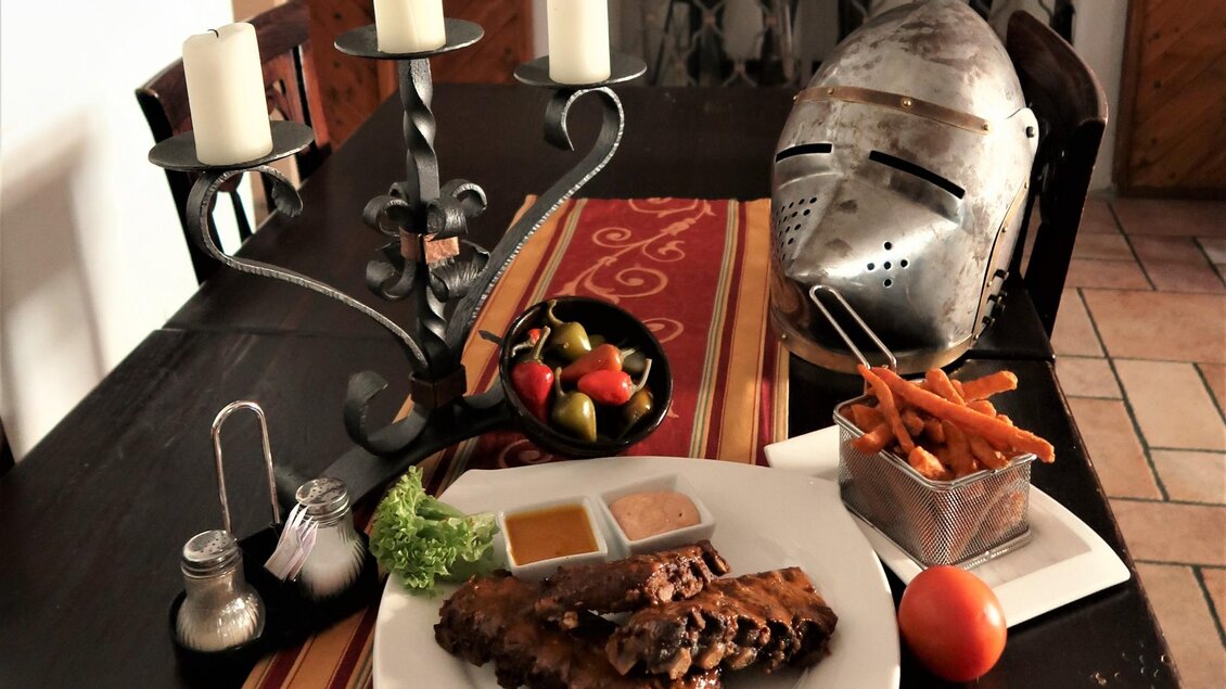Ein Tisch gedeckt mit verschiedenen Speisen und einem Kerzenständer. Im Hintergrund liegt ein Ritterhelm. | © Ritterwirt