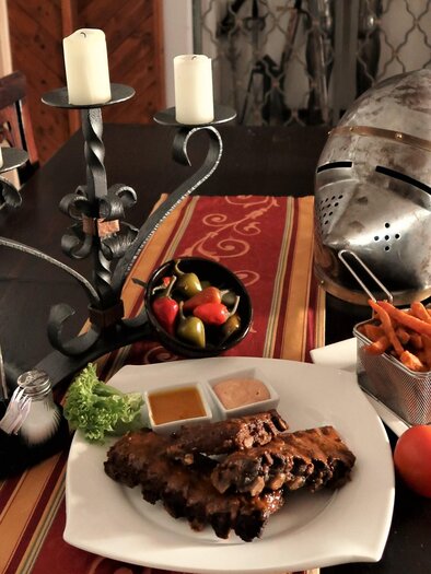 Ein Tisch gedeckt mit verschiedenen Speisen und einem Kerzenständer. Im Hintergrund liegt ein Ritterhelm. | © Ritterwirt