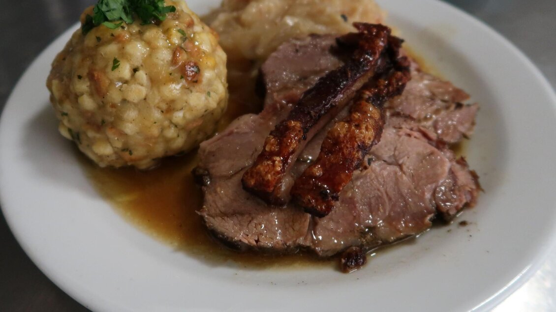 Ein Teller mit zartem Fleisch, serviert mit knusprigem Speck und einem großen Knödel. Daneben befindet sich eine Portion Kartoffelbrei. | © Ritterwirt