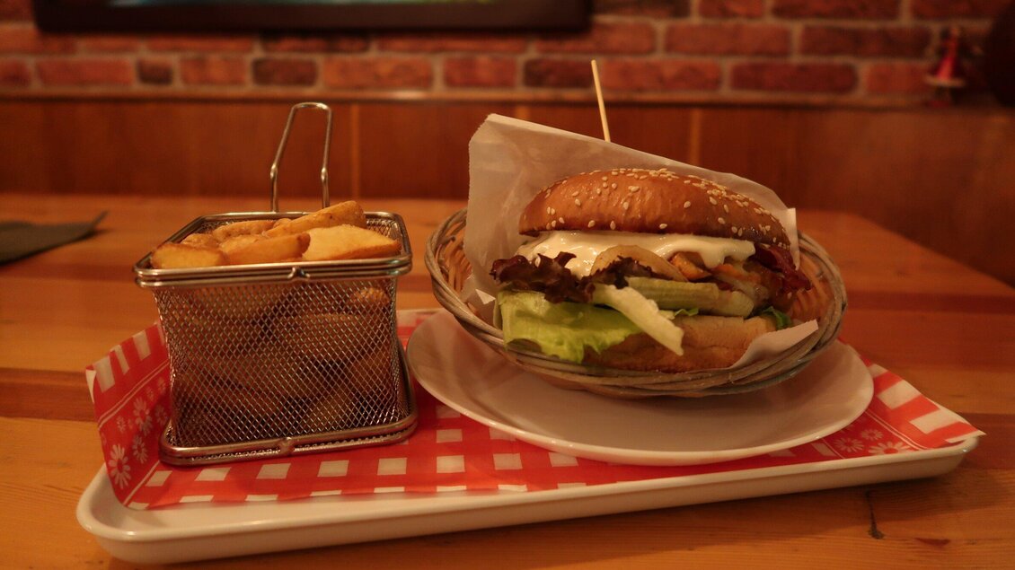 Ein köstlicher Burger mit Salat und Sauce auf einem Teller. Dazu gibt es eine kleine Frittierkörbchen mit Pommes. | © Ritterwirt