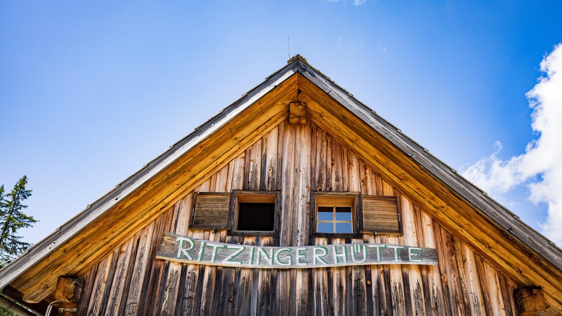 Ein traditionelles Holzhaus mit einem spitzen Dach. Über dem Eingang steht der Schriftzug "Ritzingerhütte". | © Netzwerk Kulinarik Wildbild