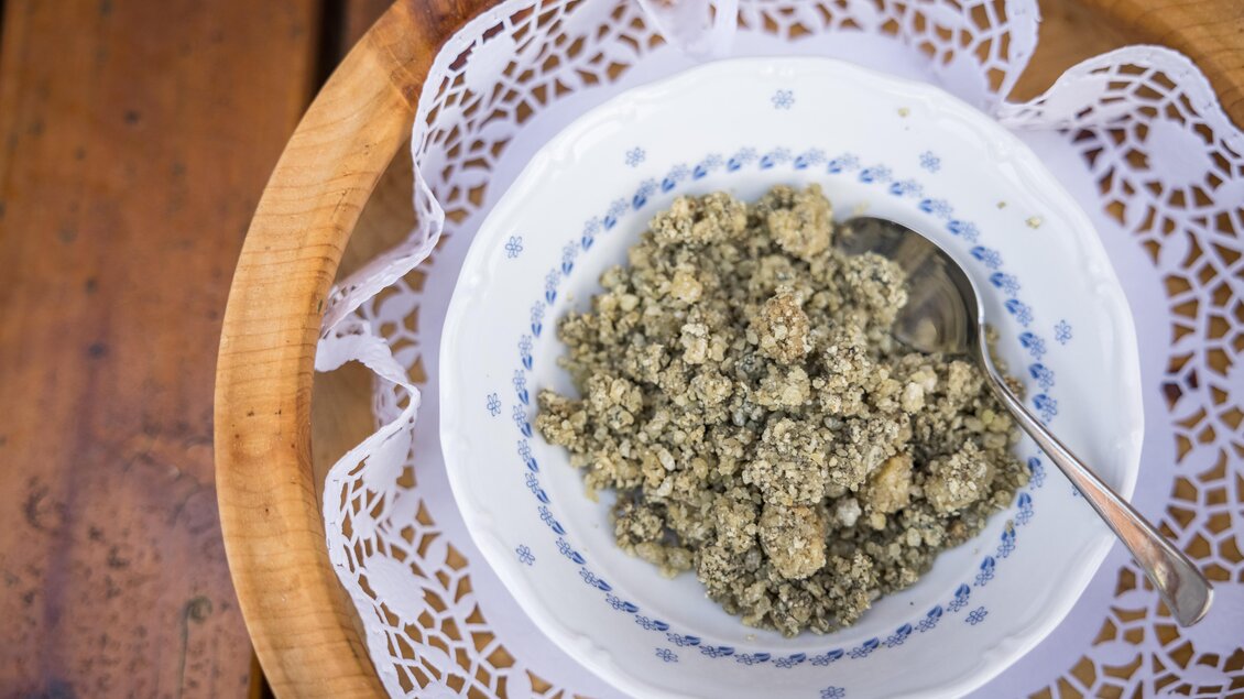 Eine Schüssel mit einer graugrünen Mischung steht auf einem schlichten Tablett. Es sieht aus wie eine Art Pudding oder Brei und ist mit einem Löffel serviert. | © Netzwerk Kulinarik Wildbild