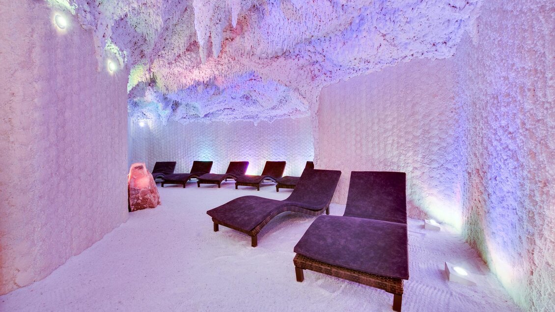 Ein entspannender Salzraum mit gemütlichen Liegen. Die Wände sind mit Salz bedeckt und sanfte Lichtfarben schaffen eine beruhigende Atmosphäre. | ©  Rogner Bad Blumau