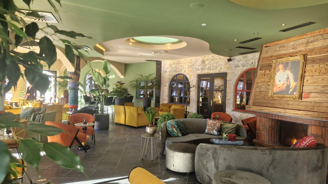 Eine moderne Lounge mit gemütlichen Sitzbereichen und einer einladenden Atmosphäre. Große Fenster und Pflanzen verleihen dem Raum ein frisches Ambiente. | © Rogner Bad Blumau/Hundertwasser Architekturprojekt