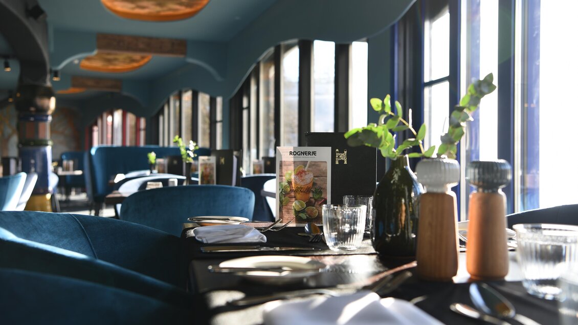 Ein stilvolles Restaurant mit blauen Möbeln und großen Fenstern. Die Tische sind elegant gedeckt und bieten eine einladende Atmosphäre. | © Rogner Bad Blumau/Hundertwasser Architekturprojekt