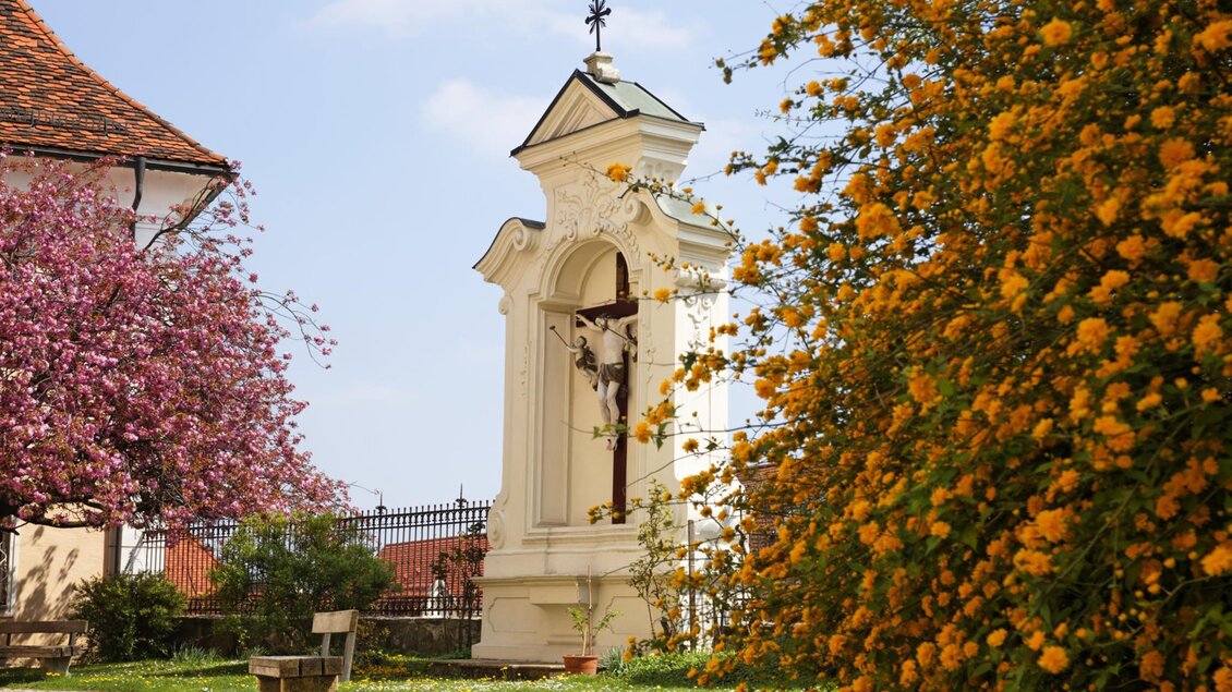 Eine malerische Szenen von einer kleinen Kapelle, umgeben von blühenden Bäumen und bunten Blumen. Der Himmel ist klar und die Atmosphäre ist friedlich. | © Tourismusverband Oststeiermark