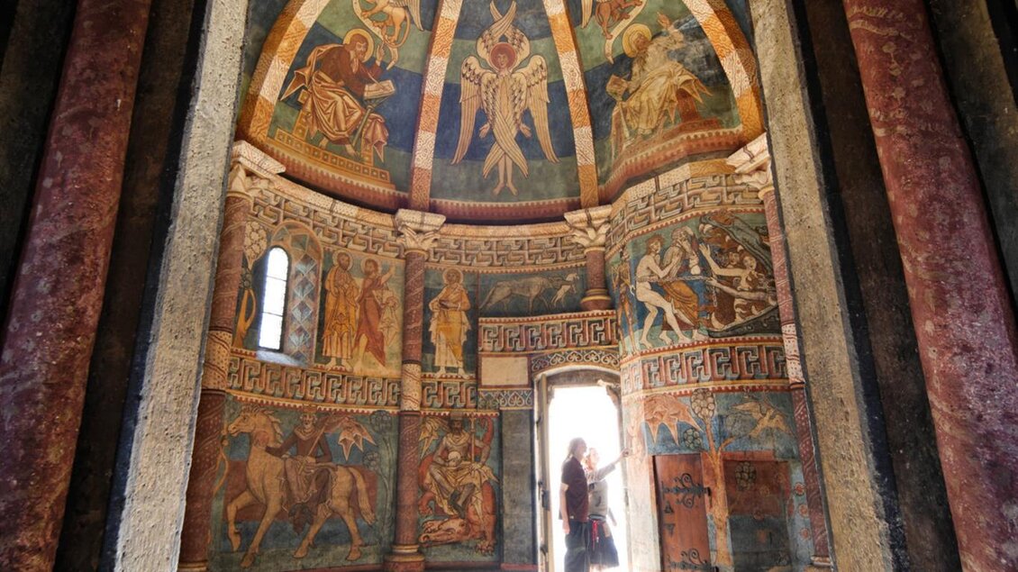 Ein historischer Innenraum mit bunten Wandmalereien und einem kunstvoll gestalteten Gewölbe. Das Licht fällt durch die Tür und beleuchtet den Raum. | © Tourismusverband Oststeiermark