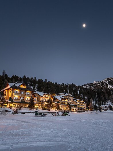 A snowy landscape with charming mountain hotels. The clear night sky shines over the snow-covered trees and mountains. | © Romantik Seehotel Jägerwirt