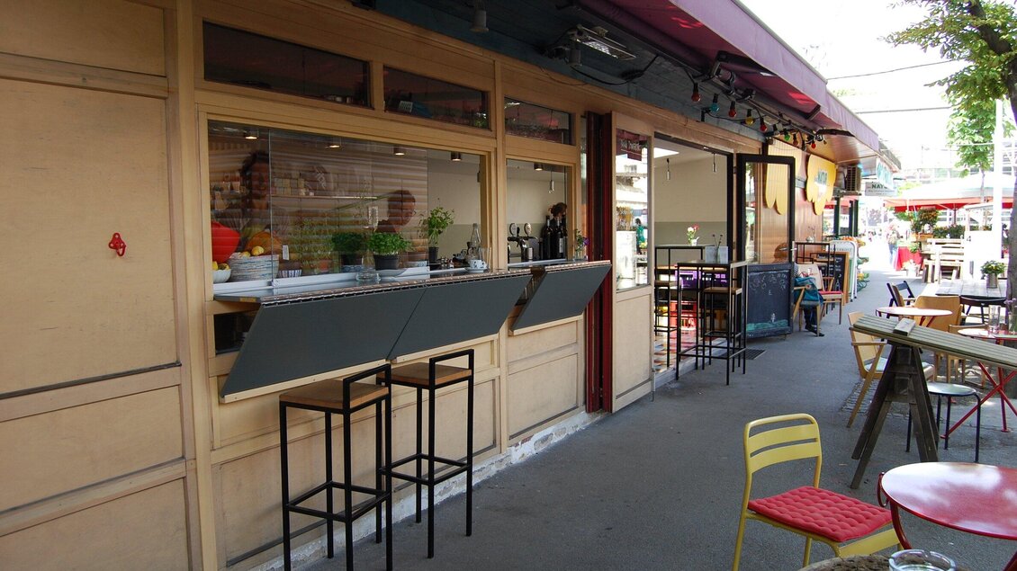 Ein modernes Café mit offenen Fenstern und Stühlen auf der Straße. Die Umgebung ist hell und einladend. | © Rossian