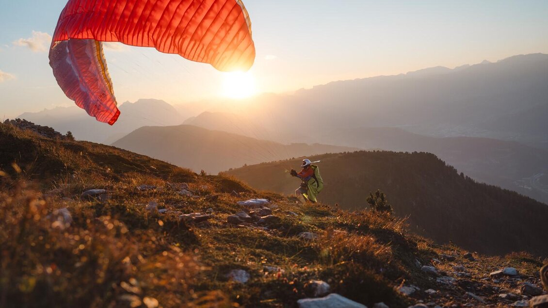 Ein Paraglider hebt in der Abenddämmerung ab. Im Hintergrund sind sanfte Hügel und ein wunderschöner Sonnenuntergang zu sehen. | © Christoph Lukas