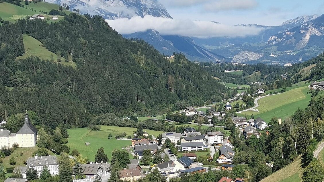 Eine malerische Berglandschaft mit grünen Wiesen und einem kleinen Dorf. Im Hintergrund sind majestätische Berge und ein klarer blauer Himmel zu sehen. | © Landentwicklung Steiermark