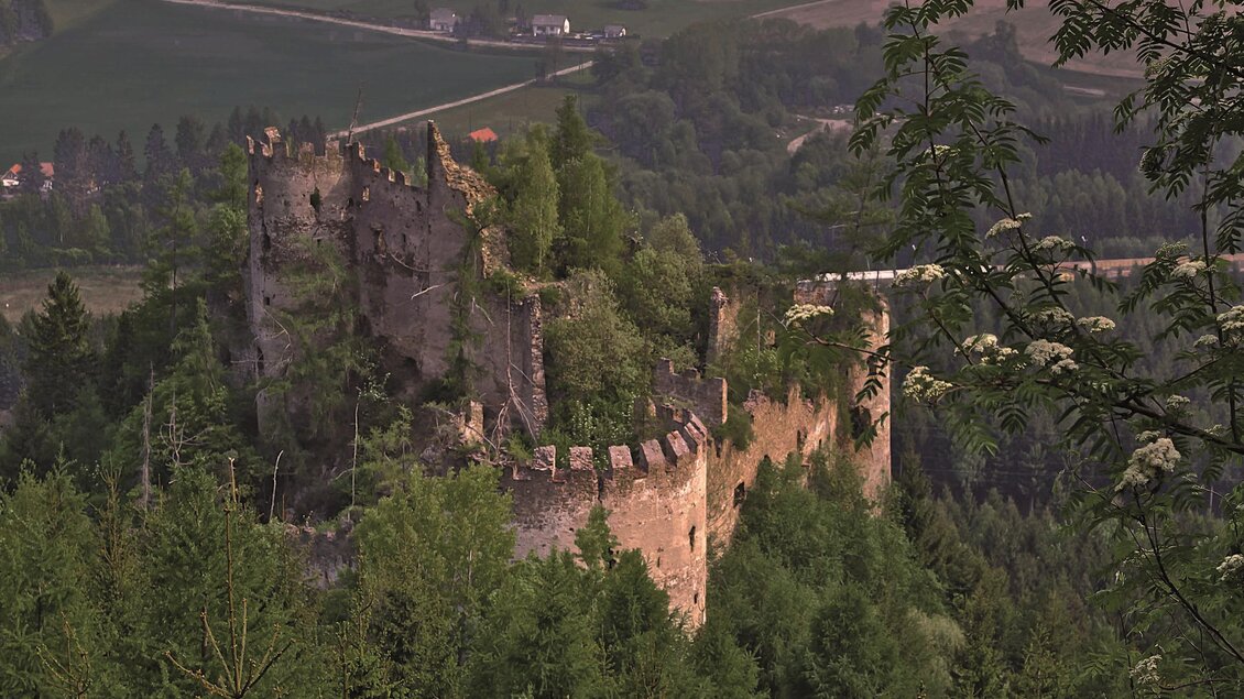 Eine alte Burgruine umgeben von grünen Bäumen. Im Hintergrund sind sanfte Hügel und eine ländliche Landschaft sichtbar. | © Markus Beren