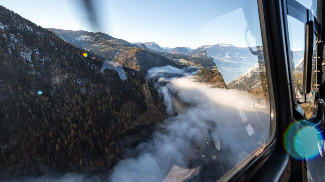 Eine atemberaubende Aussicht auf Berge und Nebel von einem Fenster aus. Der Himmel ist klar und die Landschaft ist von üppigem Grün und Wäldern geprägt.